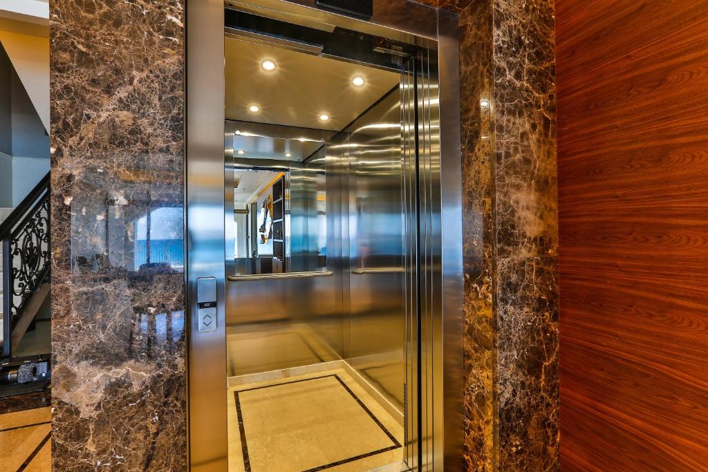Mūsdienīgs lifts ar spīdīgām nerūsējošā tērauda durvīm, kas ierīkots elegantā interjerā ar akmens un koka apdari.