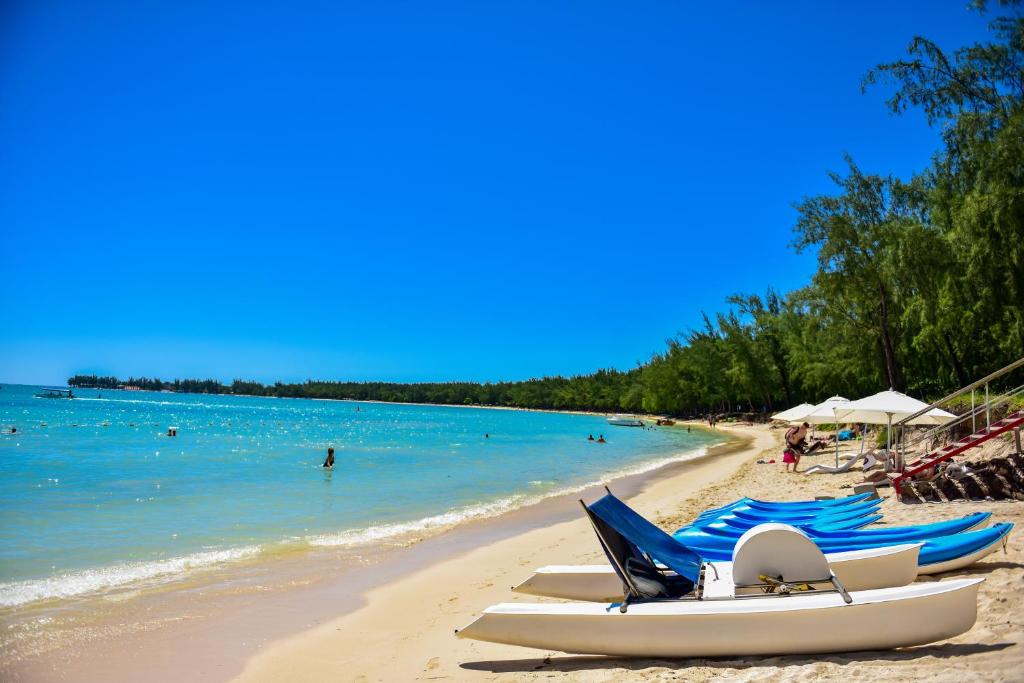 Piekraste ar smiltīm un zilu ūdeni, kur atpūšas cilvēki un stāv laivas. Ideāla vieta brīvā laika pavadīšanai un pludmales aktivitātēm.
