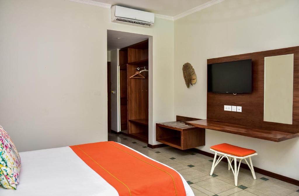 Mūsdienīga viesnīcas istaba ar gultu, televizoru un koka mēbelēm, kas rada mājīgu atmosfēru. Uzsvars uz minimalistisku dizainu un ērtībām.