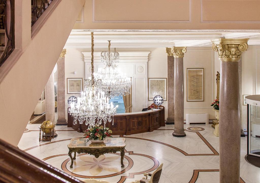 Grezna viesnīcas recepcija ar elegantu kristāla lustru un greznu interjeru, akcentēta ar kolonnām un mākslas darbiem. Ideāla vieta, lai uzņemtu viesus un radītu patīkamu atmosfēru.