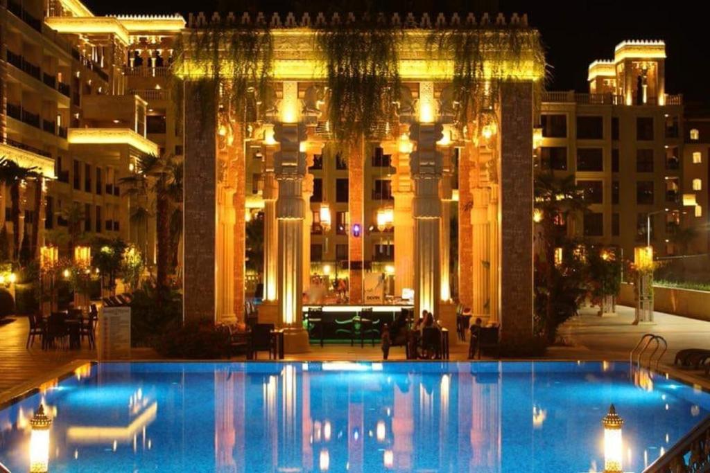 Moderns viesnīcas komplekss ar elegantu arhitektūru un apgaismotu baseinu, kas atspoguļo nakts gaismu. Apkārtējie augi un terases rada patīkamu atmosfēru.