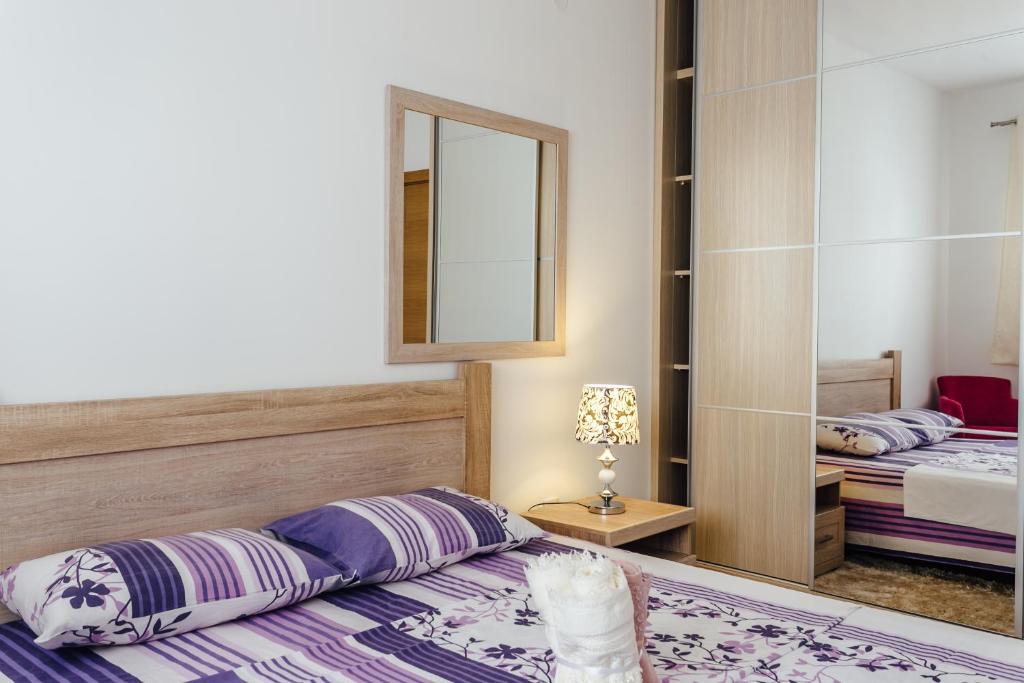 Mūsdienīgs guļamistabas interjers ar koka gultu un spilgtu gultas veļu, spoguli un naktslampu. Siltas krāsas un ērtības rada relaksējošu atmosfēru.