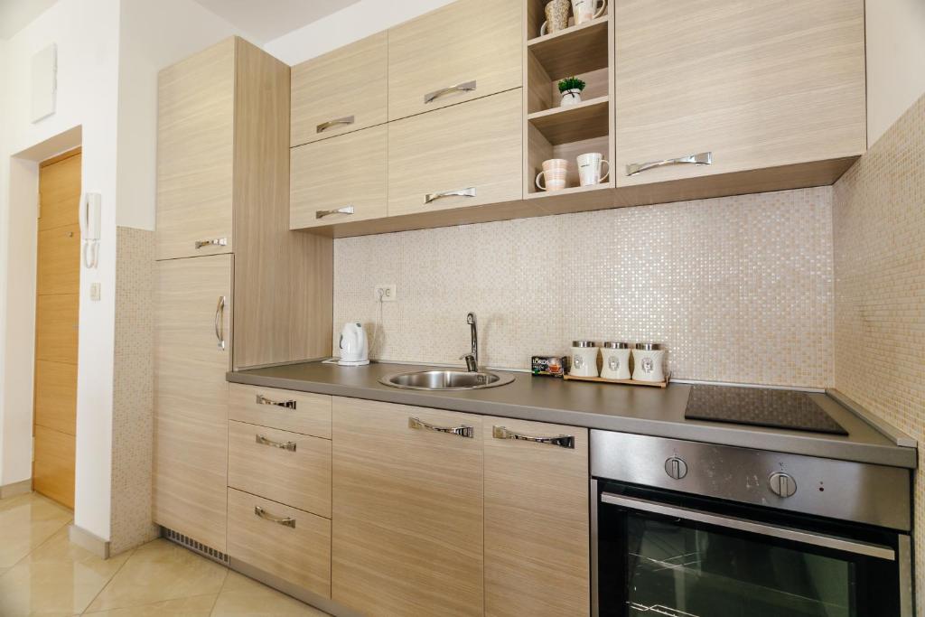 Mūsdienīgs virtuve ar koka skapjiem, metāla virsmu un sīkrīkiem, kas iekārtota ar gaišām, neitrālām krāsām. Interjers ir funkcionāls un elegants, radot patīkamu atmosfēru.