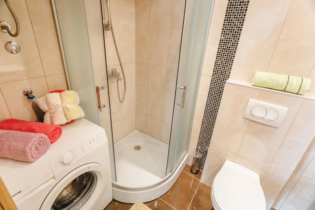 Kompakta vannas istaba ar dušu, veļas mašīnu un krāsainām dvieļiem, kas rada mājīgu un funkcionālu atmosfēru.