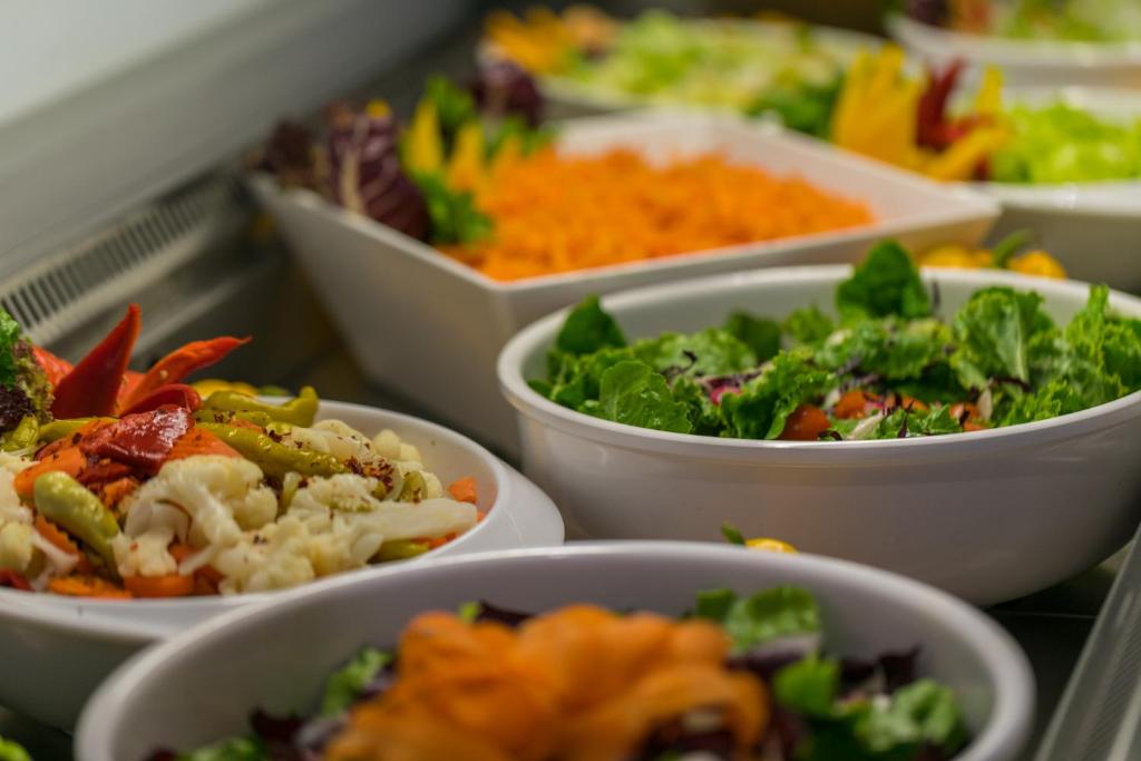 Dažādu salātu un dārzeņu bļodas, kas sakārtotas uz galda, piedāvājot veselīgu un krāsainu ēdienu izvēli.