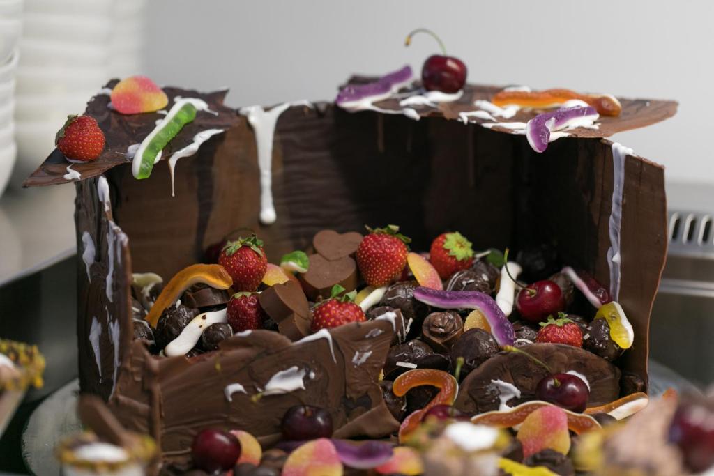 Šokolādes kastīte, piepildīta ar augļiem un saldumiem, dekorēta ar krāsainiem konfektēm un šokolādes izstrādājumiem. Šī saldā delikatese ir lielisks deserts svinībām.