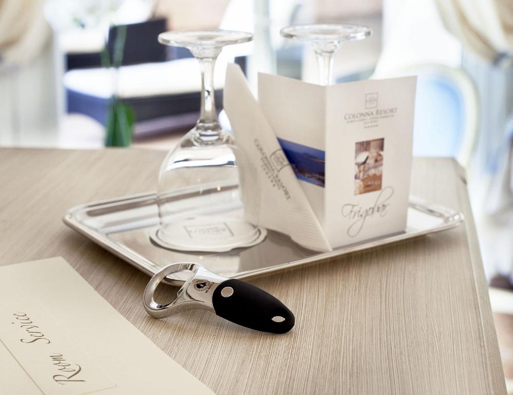 Elegants galda iestatījums ar sudraba paplāti, divām glāzēm, viesnīcas ēdienkarti un pudeļu atkorķētāju. Ideāls skats uz viesnīcas apkalpošanu un relaksāciju.