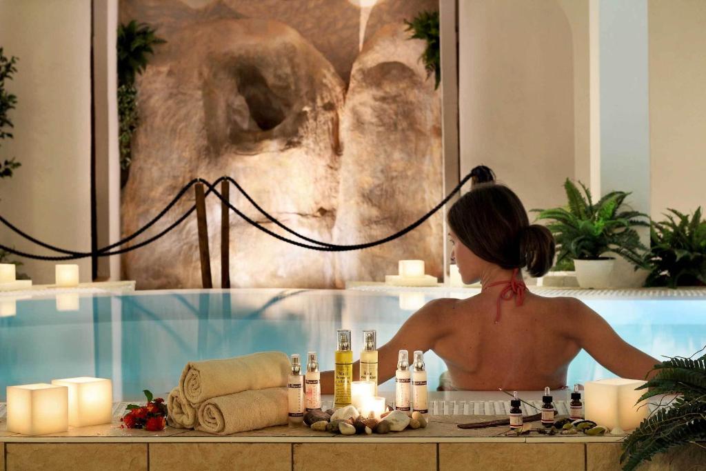 Relaksējoša spa vide ar personu, kas atpūšas baseinā, apkārt ir aromātiskas eļļas un sveces. Daba un harmonija veido mierīgu atmosfēru.