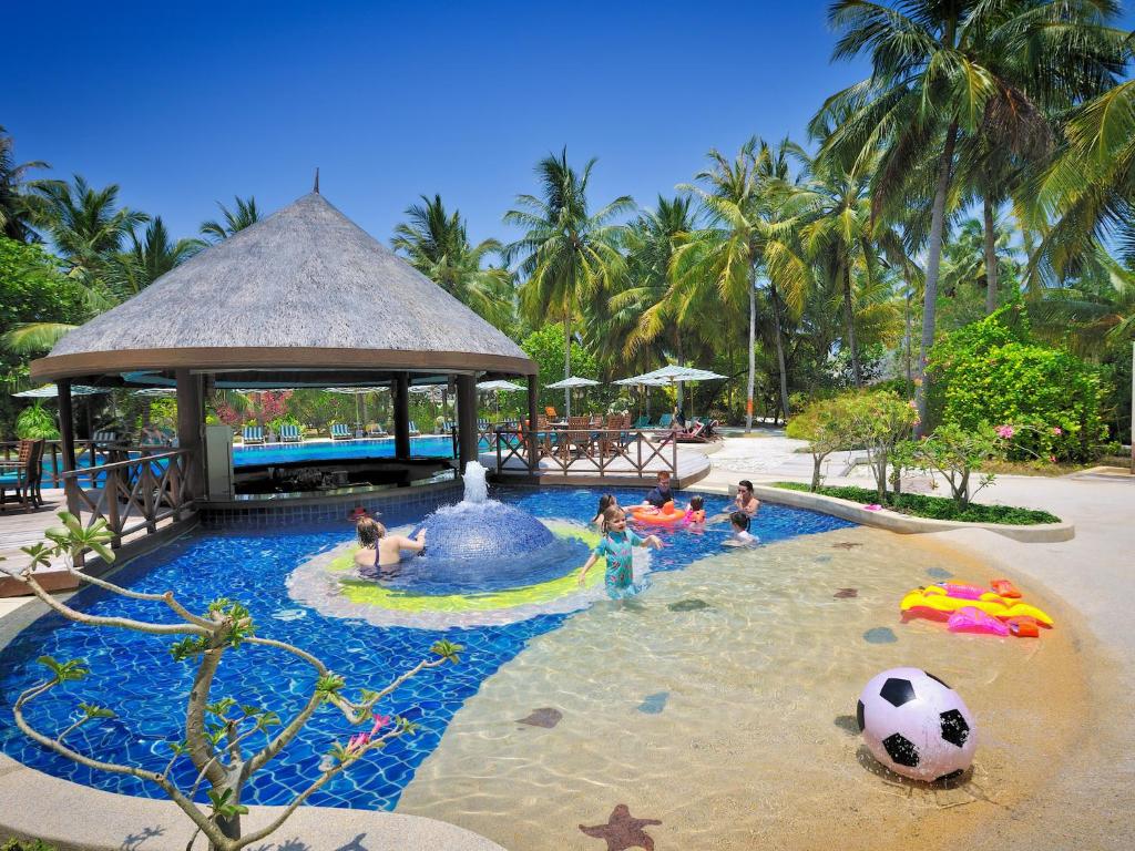Atpūtas komplekss ar bērnu baseinu, kur bērni spēlējas un izbauda ūdeni, apkārt palmām un atpūtas zonām. Ideāla vieta ģimenes brīvdienām.