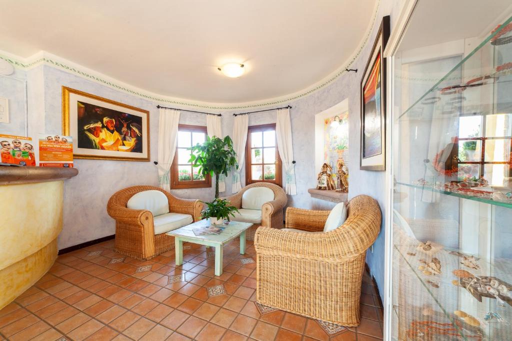 Mājas interjers ar vīna krāsā apgleznotām sienām, ratanas mēbelēm un zaļo augu centrā. Telpā ir lieli logi, caur kuriem ieplūst dabiska gaisma, un redzami dekoratīvi elementi.