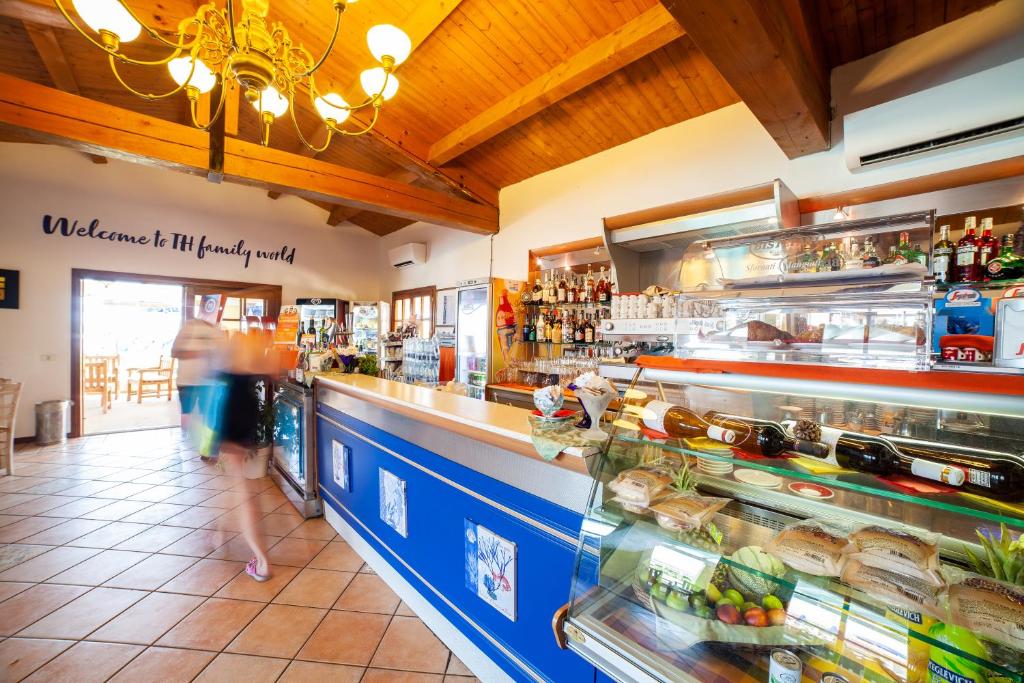 Restorāna interjers ar koka griestiem un bagātīgu dzērienu izvēli. Virs letes redzama uzraksts "Welcome to TH family world", kas rada viesmīlīgu atmosfēru.