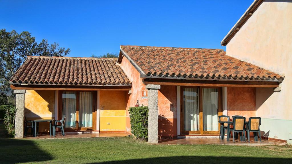 Mājas ēka ar krāsainām sienām un flīžu jumtu, apkārt esošu zāli un terasi, kurā ir galdi un krēsli. Ideāla vieta atpūtai un relaksācijai.