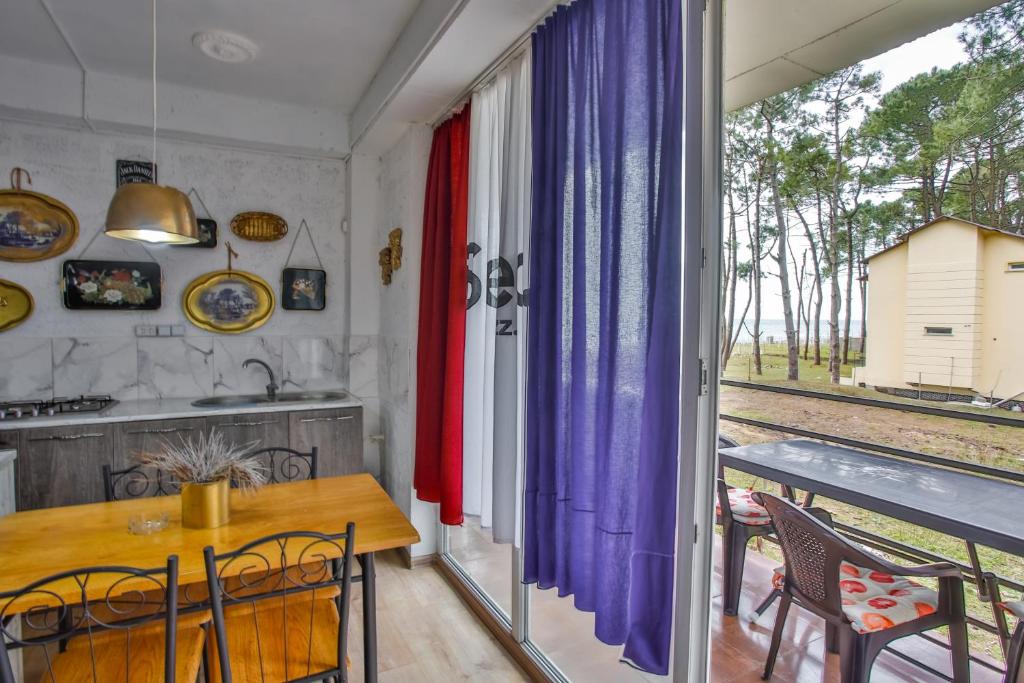 Mūsdienīga virtuve ar koka galdu un krēsliem, dekorēta ar vintage mākslas darbiem un krāsainām aizkariem, kas piedāvā skatu uz dārzu un mežu.