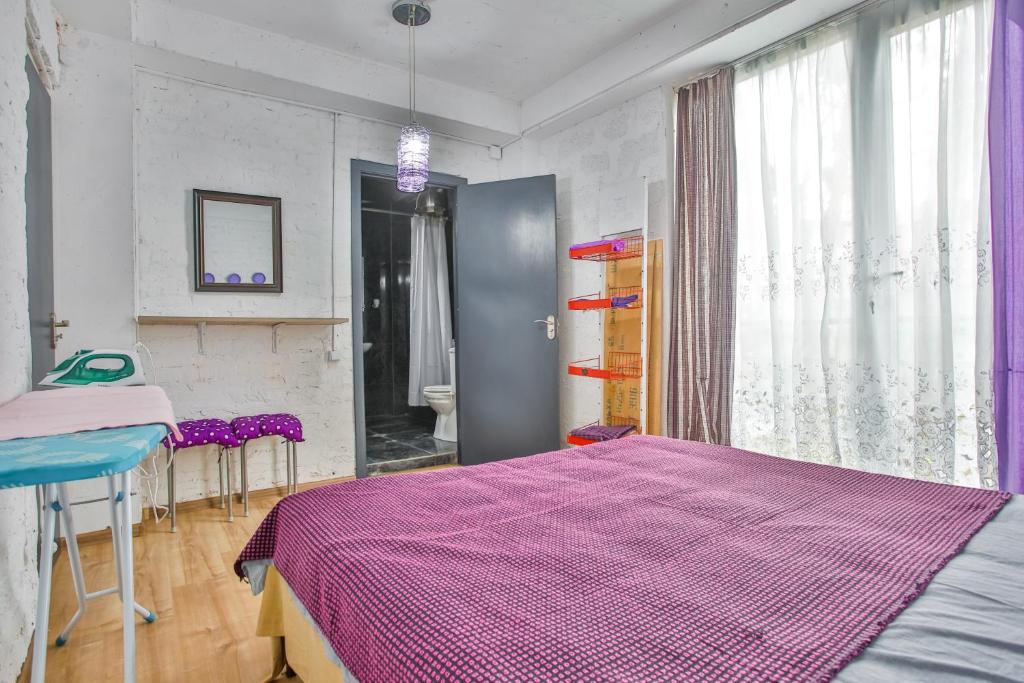 Moderns guļamistabas interjers ar gultu, dīvānu un skatu uz vannas istabu. Telpā ir gaišas krāsas un mūsdienīgi aksesuāri, piemēram, gludeklis un plaukti.