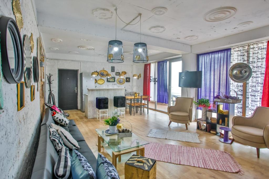 Moderns viesistabas interjers ar stilīgu mēbeļu izkārtojumu, dekoratīvām spoguļu rāmēm un krāsainām aizkaru drānām. Telpā ir liels logs, kas nodrošina dabisko apgaismojumu.