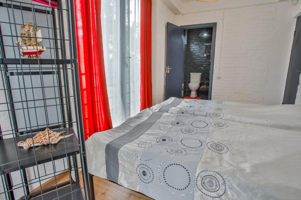 Gultas istaba ar sarkaniem aizkariem, modernu dizainu un piekļuvi vannas istabai. Uz naktsgaldiņa ir dekoratīvs priekšmets.