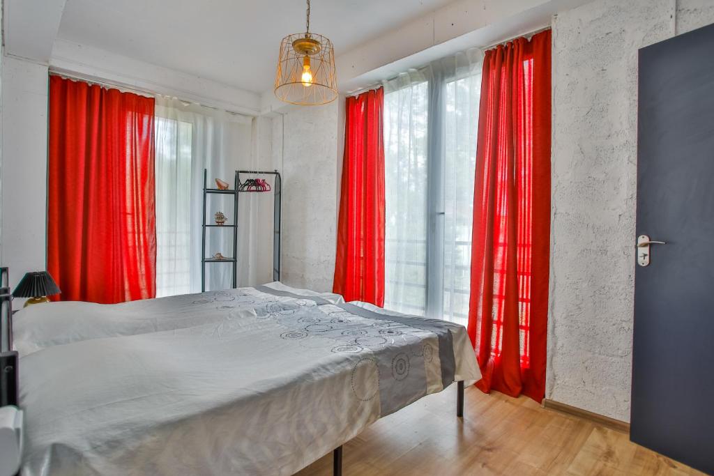 Mūsdienīgs guļamistabas interjers ar gaišām gultām un sarkaniem aizkariem, kas piešķir dzīvīgu akcentu. Telpa ir labi apgaismota ar dabiskiem gaismas avotiem.