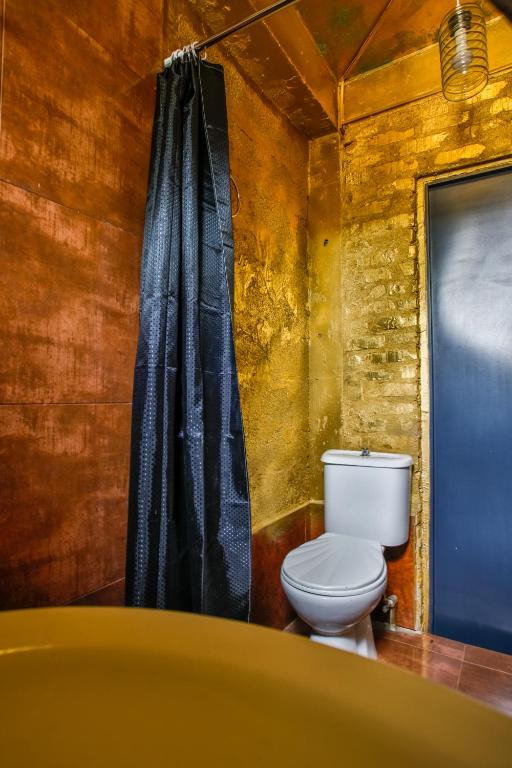 Moderns vannas istabas interjers ar zeltainām sienām, melnu dušas aizkaru un baltu tualeti. Elegants dizains, kas apvieno luksusu un funkcionalitāti.