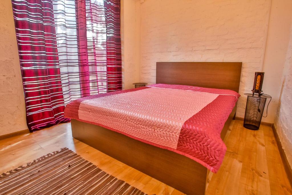 Guļamistaba ar koka gultu un rozā pārklāju, ko rotā logi ar sarkaniem un baltajiem svītrojumiem. Telpu papildina moderna apgaismojuma elements un koka grīda.