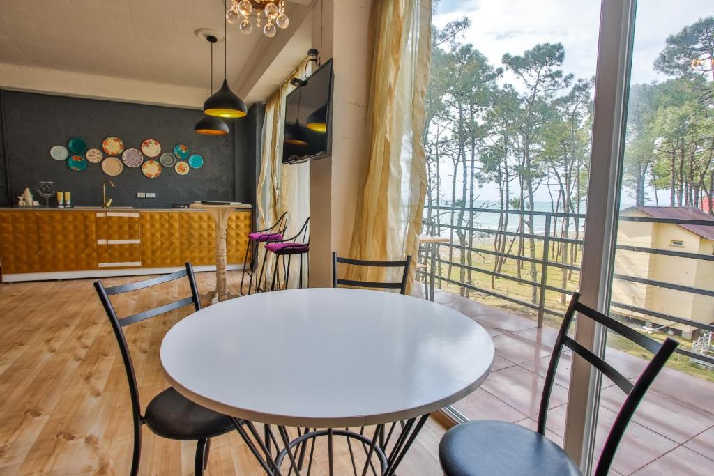 Moderns interjers ar baltu galdu un skatu uz dabu, kurā redzams koka grīdas un stilīgs virtuves izkārtojums. Gaismas elements un dekoratīvas plāksnes piešķir telpai raksturu.