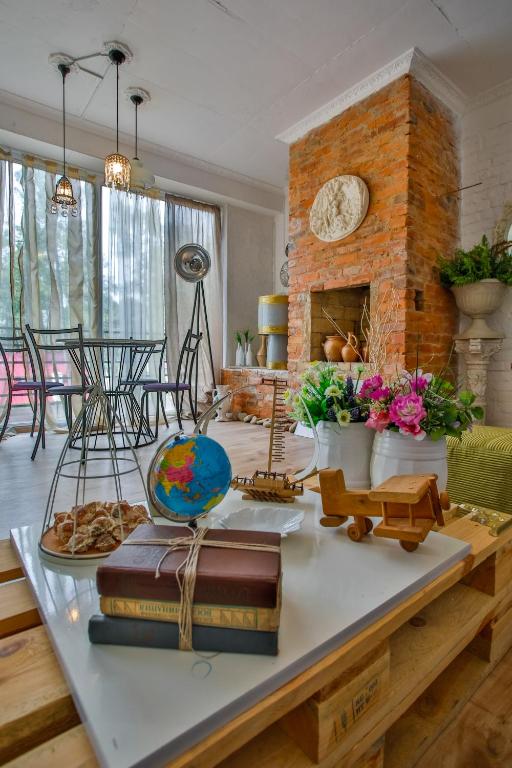 Mūsdienīga viesistaba ar sarkanu ķieģeļu kamīnu, dekoratīvām ziedu kompozīcijām un vintage elementiem, piemēram, globusu un kuģi. Gaismas plūst caur logiem, radot patīkamu atmosfēru.