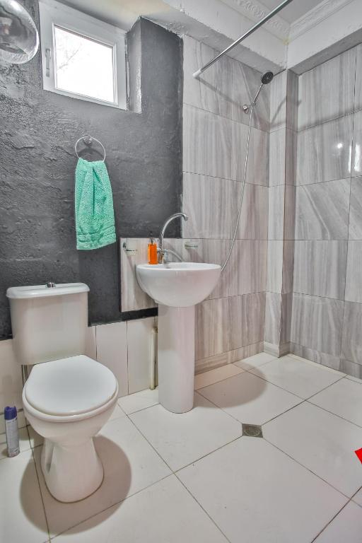 Mūsdienīga vannas istaba ar pelēkām flīzēm, balto izlietni un tualeti. Telpā ir duša ar stikla sienu un logu, kā arī zaļš dvielis uz āķa.