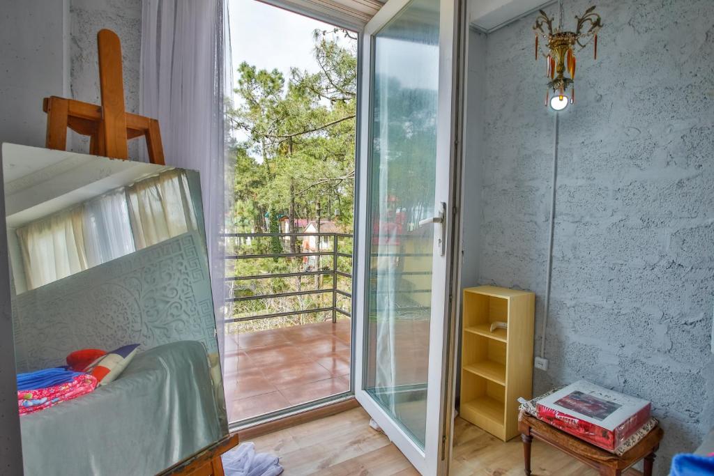 Gaismas un mākslas atmosfēra telpā ar logu un balkonu, kur redzami koki un dārza skats. Iekārtota ar spoguli un vienkāršu mēbelēm, radot mājīgu un radošu vidi.