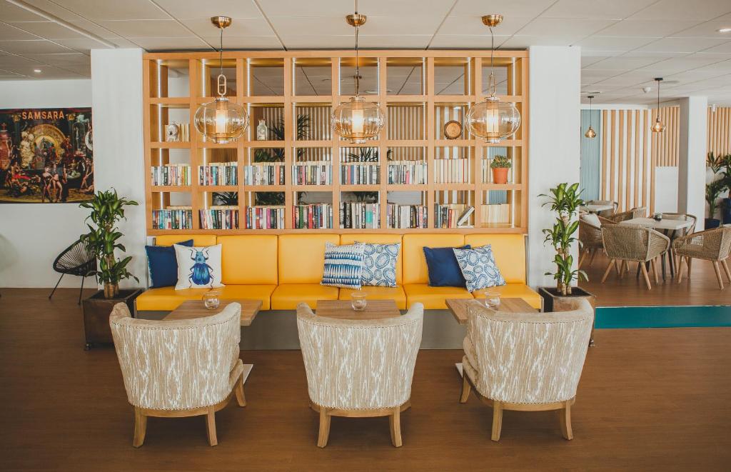 Mūsdienīga atpūtas zona ar dzeltenu dīvānu un elegantām krēsla grupām, kas rotāta ar grāmatām un augiem. Interjers ir gaišs un viesmīlīgs, radot patīkamu atmosfēru.