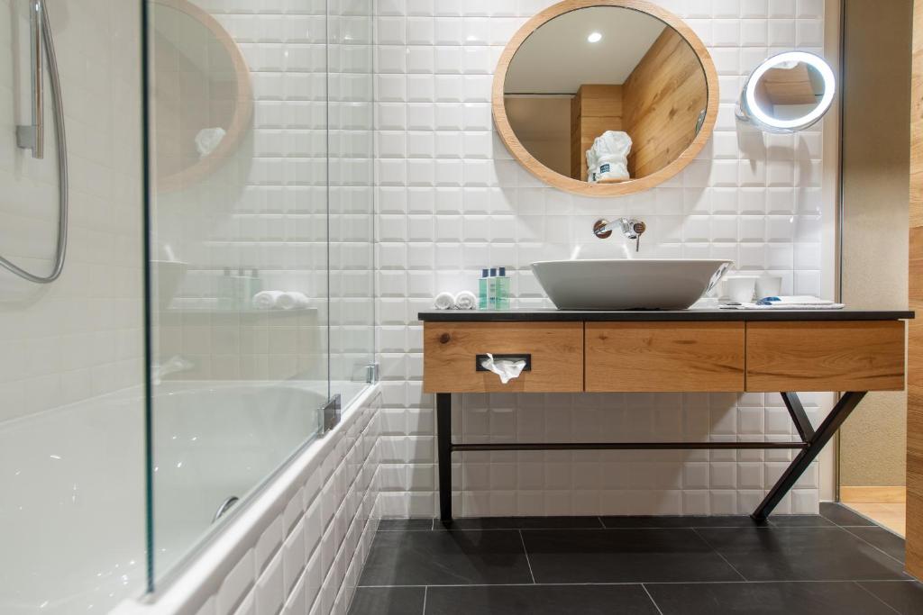 Mūsdienīgs vannas istabas interjers ar melnu flīžu grīdu, koka izlietni un apaļu spoguli, kas radījis elegantu un tīru izskatu.