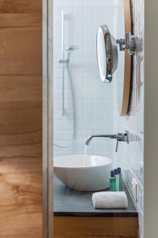 Mūsdienīgs vannas istabas interjers ar peldošu izlietni un higiēnas līdzekļu komplektu. Sienas ir klātas ar gaišiem flīzēm, un redzama ir arī dušas kabīne.