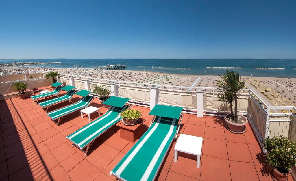 Saulaina pludmales terase ar zaļām sauļošanās krēslām un skatu uz jūru, kur redzami smilšaini krasti un sauļošanās vietas. Ideāla vieta atpūtai un relaksācijai.