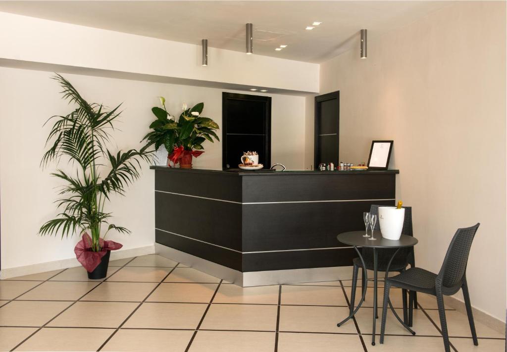 Mūsdienīgs viesnīcas reģistratūras stūris ar melnu reģistratūras letni, zaļām telpaugu kompozīcijām un ērtu galdu divām krēsliem.