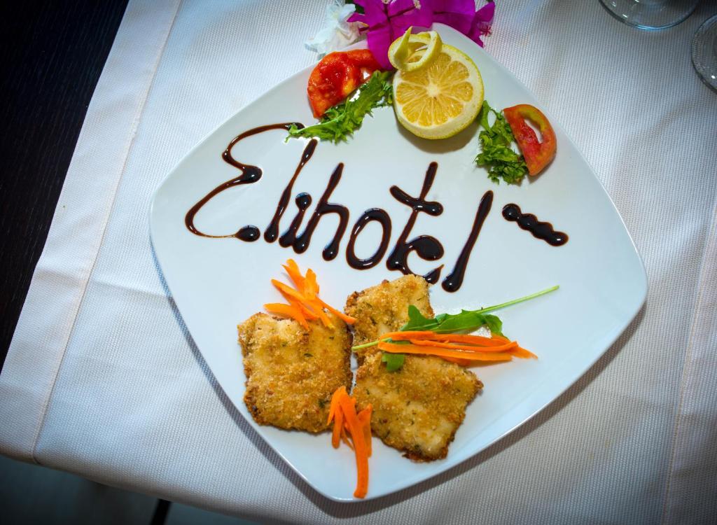 Skaisti pasniegts ēdiens ar kraukšķīgu zivi, dekorēts ar burkānu sloksnēm, salātu lapām un tomātu šķēlītēm, ar citronu un šokolādes mērci, kas veido vārdu "Elihotel."