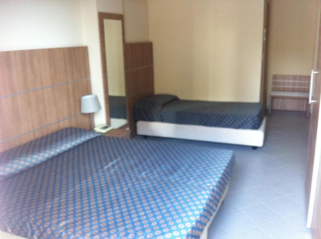 Vienkārša viesnīcas istaba ar diviem gultām, moderniem koka elementiem un spoguli. Telpa ir gaiša un plaša, radot komfortablu atmosfēru.