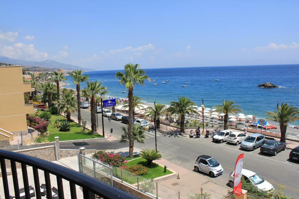 Jūras pludmale ar palmām, automašīnām un cilvēkiem, kas bauda sauli. Tuvumā redzama pludmales infrastruktūra un zils jūras ūdens.