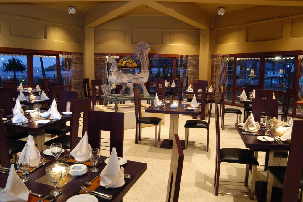 Elegants restorāns ar modernu interjeru, kurā ir eleganti galdi un krēsli, apgaismots ar siltu gaismu. Centrā atrodas dekoratīvs elements, kas piešķir atmosfēru.