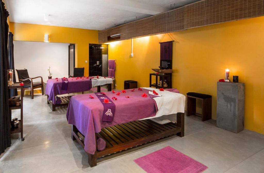 Mūsdienīgs spa telpa ar masāžas galdiem, rotātiem ar ziedlapiņām, un siltu dzeltenu sienu. Telpā ir relaksējoša atmosfēra un komfortabli sēdvietas.