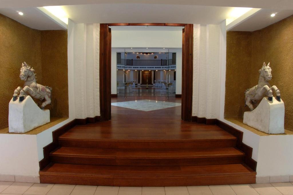Ieejas zonas attēls ar diviem akmens zirgiem abās pusēs un koka kāpnēm, kas ved uz plašu telpu. Interjers ir moderns ar siltu apgaismojumu un elegantu dizainu.