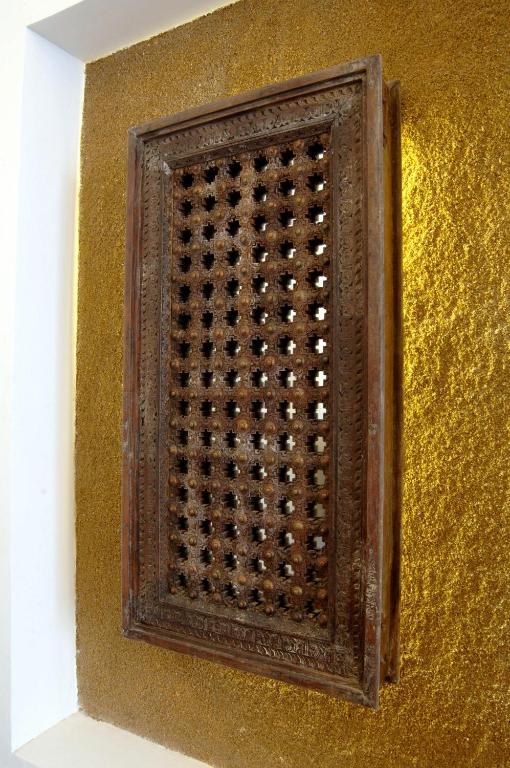 Koka paneļa ar izgriezumiem un dekoratīvu apdari attēls, kas novietots uz zeltainas fona. Paneļa sarežģītā struktūra piešķir telpai unikālu raksturu.