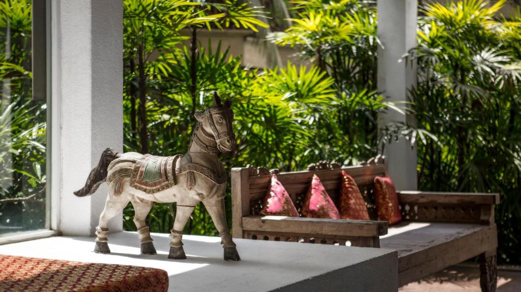 Koka zirga statuja interjerā, blakus dīvānam ar spilveniem, un apkārt zaļa augu vide.