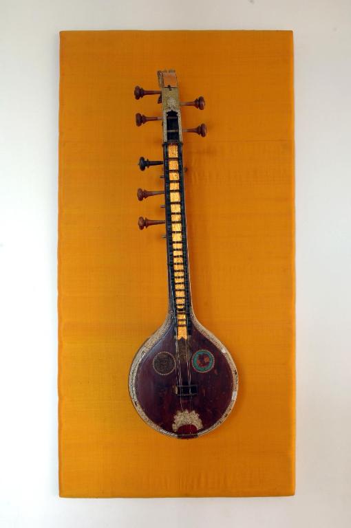 Tradicionāla indiska mūzikas instrumenta attēls ar izteiksmīgu oranžu fonu. Instruments ir dekorēts un izgatavots ar rūpīgu meistarību.