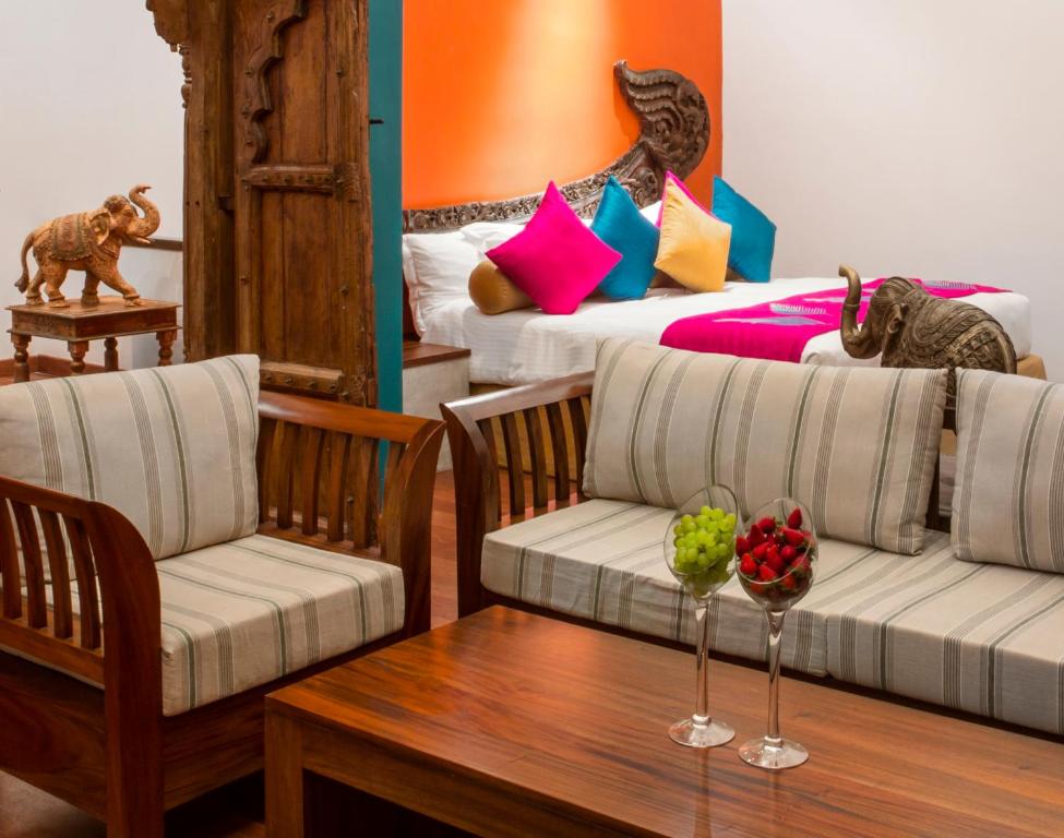 Krāsaina viesnīcas istaba ar tradicionālām rotāšanām, divām dīvāna zonām un galdu ar augļiem. Interjerā redzami koka elementi un spilgtas dekoratīvās spilvendrānas.