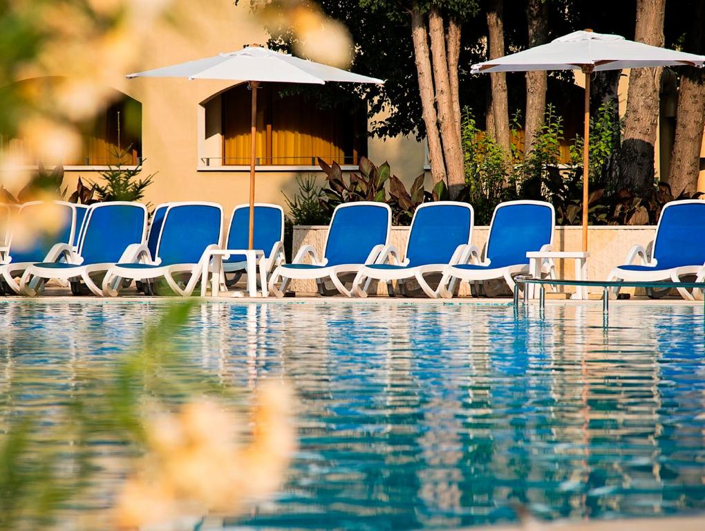 Baseins ar ziliem sauļošanās krēsliem un saules parasoliem, apkārt zaļo augi un dabiska vide.