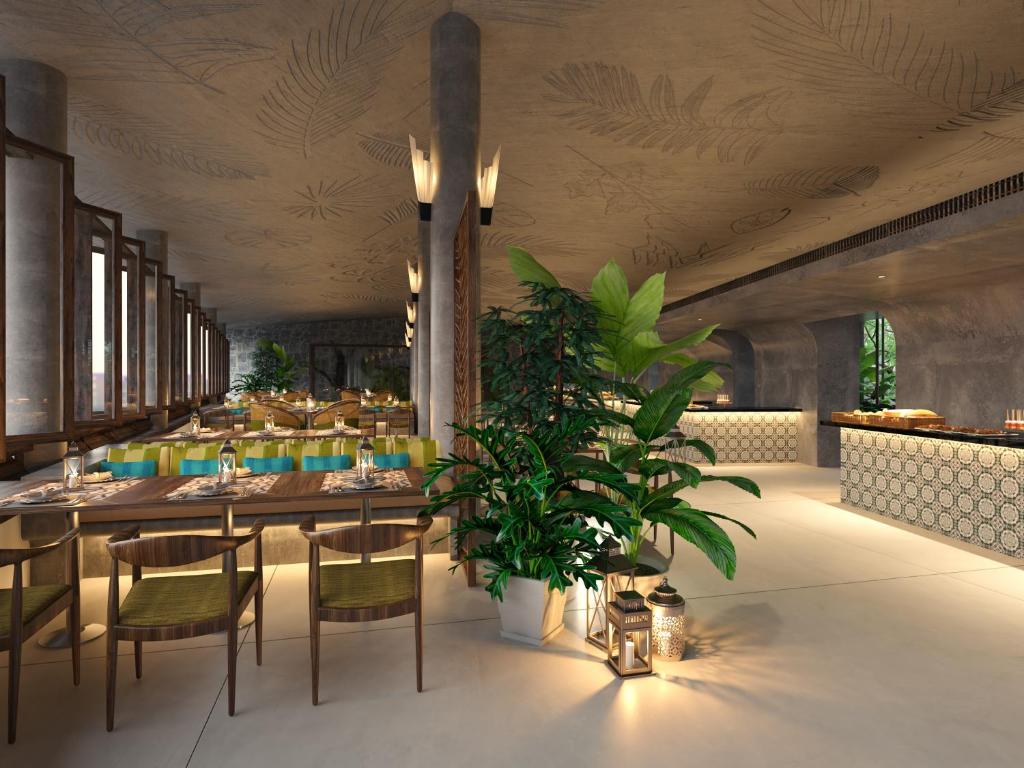 Mūsdienīgs restorāna interjers ar koka mēbelēm un zaļiem akcentiem, kas ietver augu dekorācijas un apgaismojumu. Gaisotne ir silta un aicinoša, radot patīkamu ēdiena baudīšanas pieredzi.