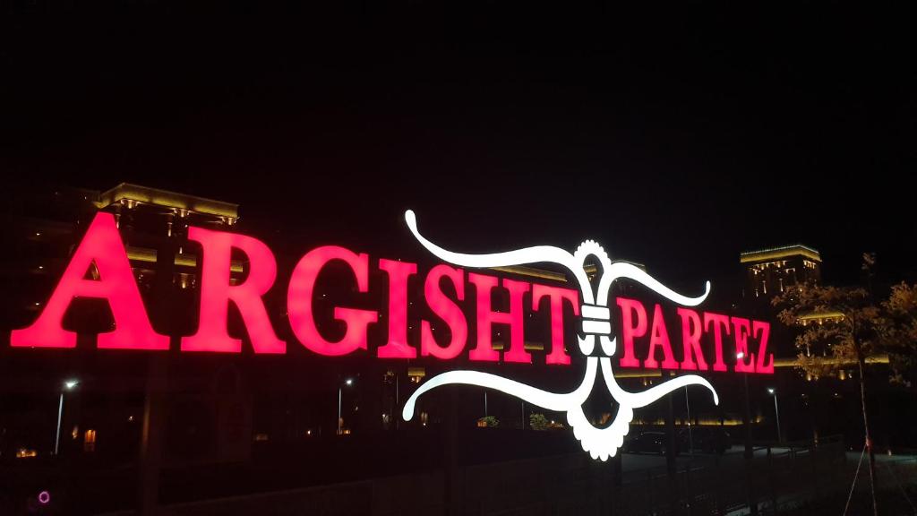 Sarkans neona reklāmas zīme "ARGISHT PARTEZ" naktī, izceļot spilgtu un pievilcīgu dizainu.