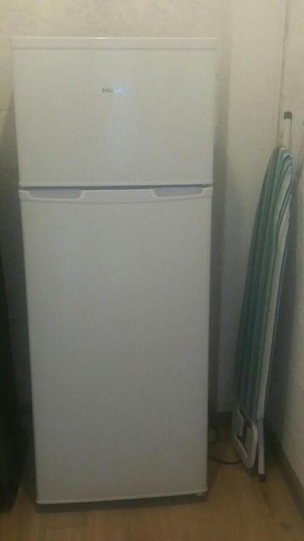 Balts ledusskapis stāv stūrī blakus gludināmo dēli ar zaļām svītrām.