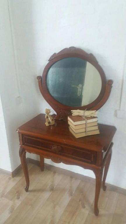 Klasisks koka tualetes galdiņš ar apaļu spoguli, uz kura novietoti grāmatu komplekti un rotaļlieta. Eleganta dizaina elementi piešķir telpai šarmu.