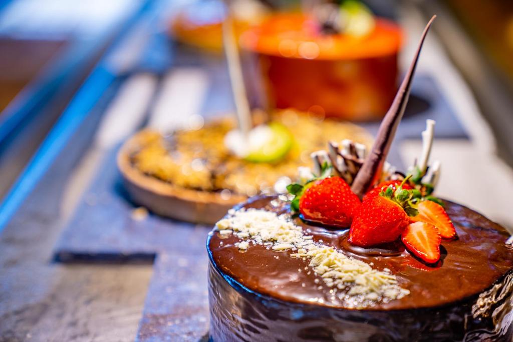 Šokolādes kūka ar zemenēm un dekoratīviem elementiem, kas izceltas uz galda blakus citām kūkām.