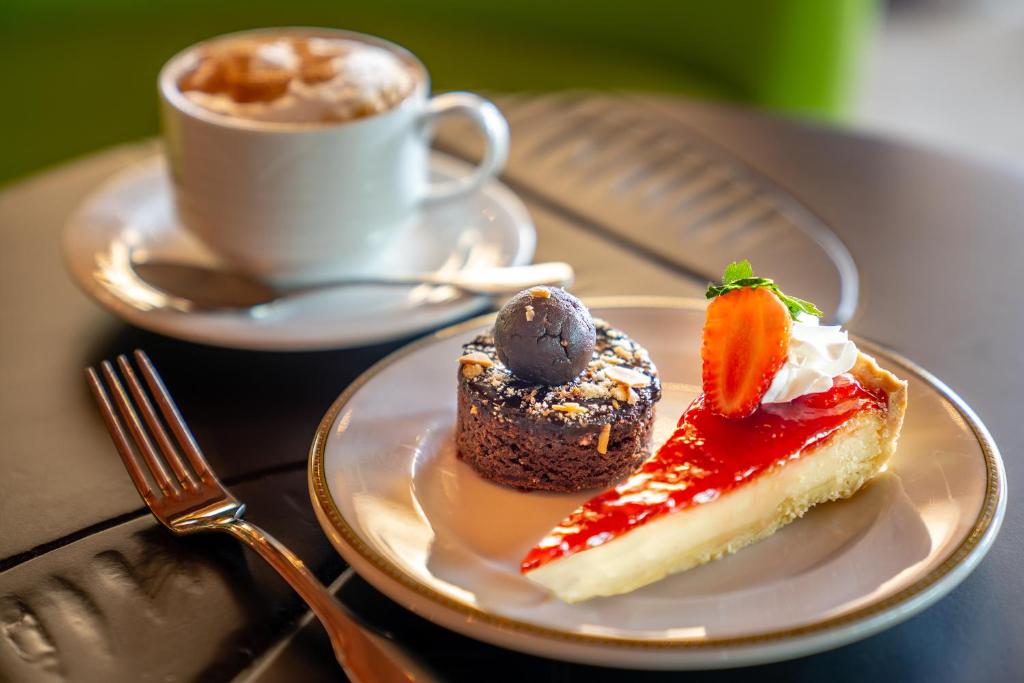 Kafijas krūze blakus desertiem, kas ietver šokolādes kūku un zemeņu pīrāgu ar krējumu.