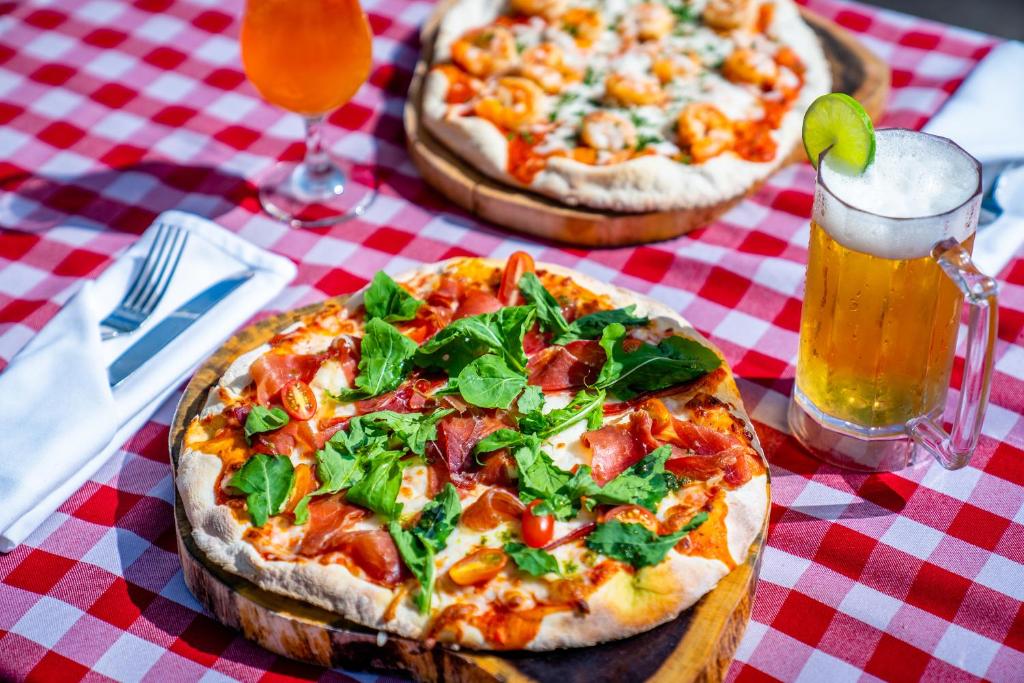 Svaiga pica ar šķiņķi un spinātiem, pasniegta kopā ar alus glāzi un dzērienu, uz sarkano un baltu pārbaudes galda.